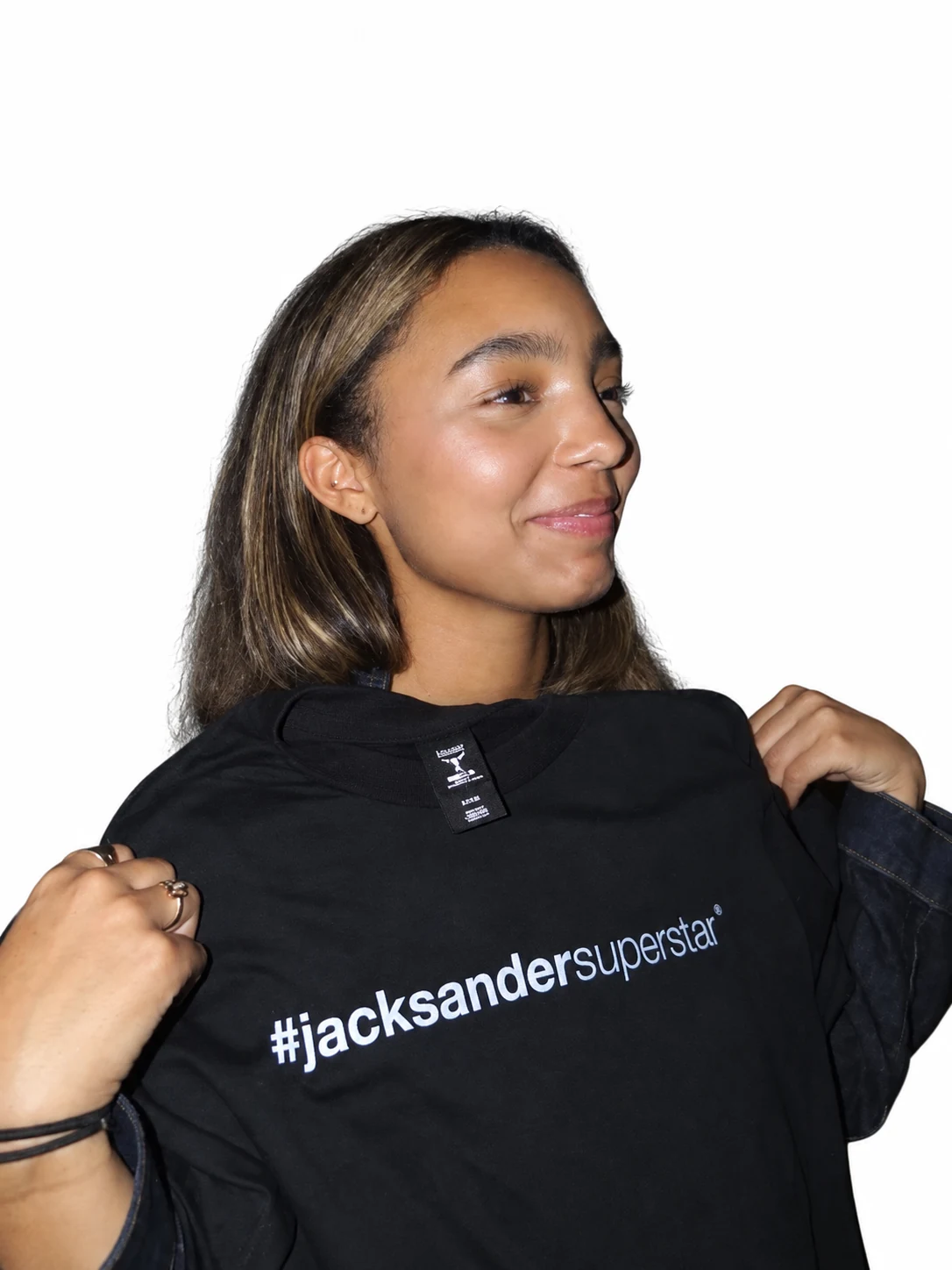 Model smiling while holding up a black jacksandersuperstar tee by its shoulders.