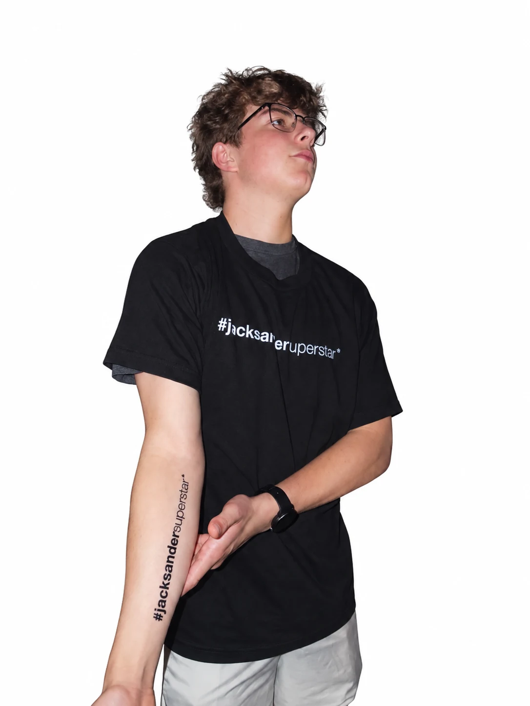 Model with glasses in a black jacksandersuperstar tee, showing the matching lettering along an outstretched forearm.