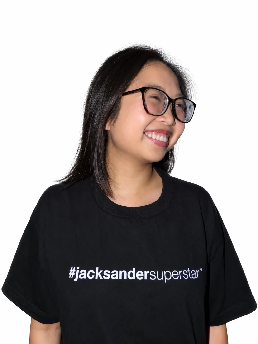 Smiling model with glasses and shoulder-length hair in a black jacksandersuperstar tee.
