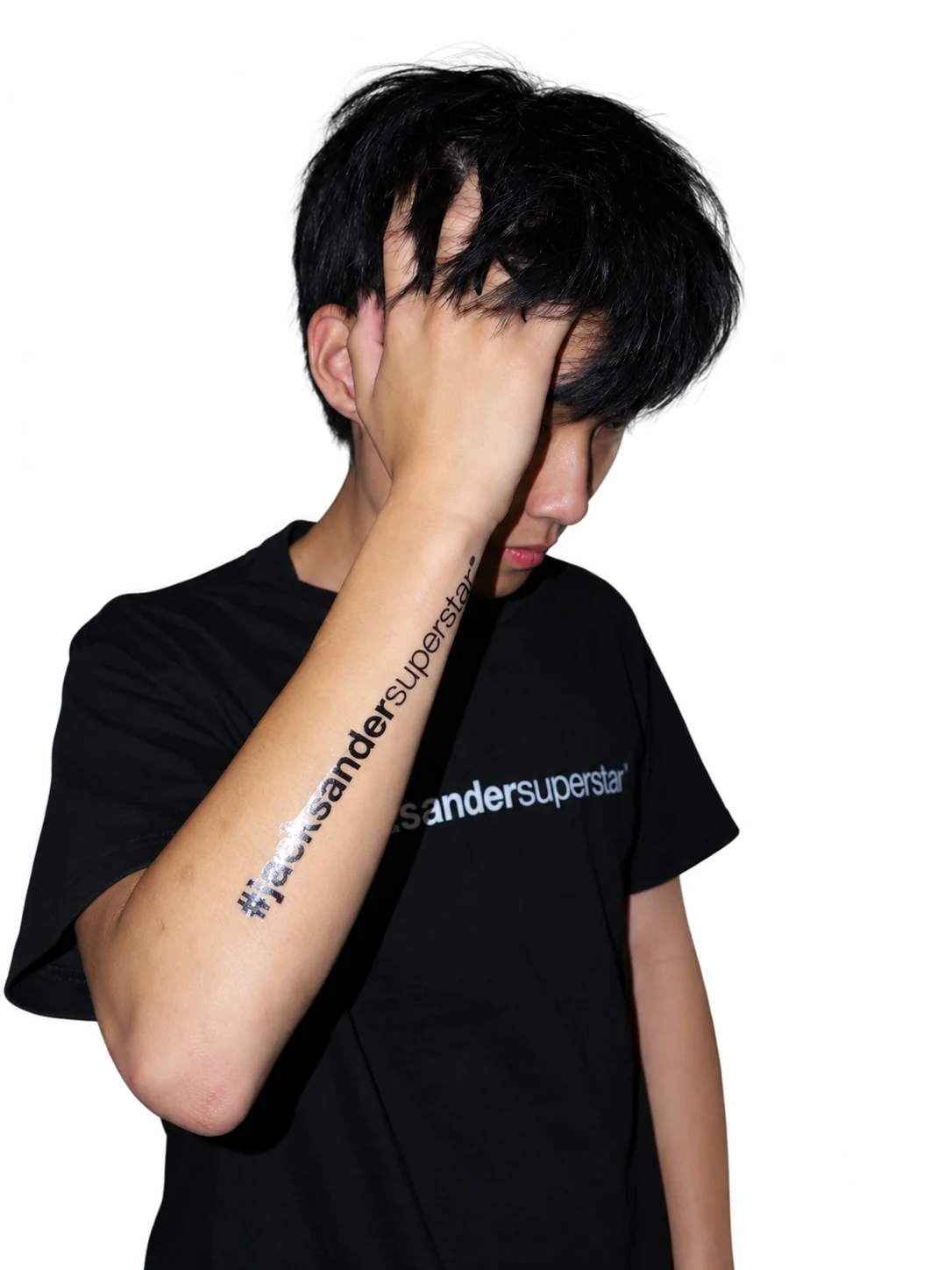 Model in a black jacksandersuperstar tee with one hand in the hair, showing matching forearm lettering.